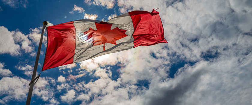 Canadian flag against a bright blue sky with white clouds