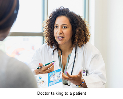 A doctor wearing a white lab coat sitting behind a desk speaks to a patient