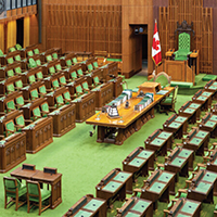 House of Commons Chamber - wooden desks and chairs with green padding facing a central divider of green carpet