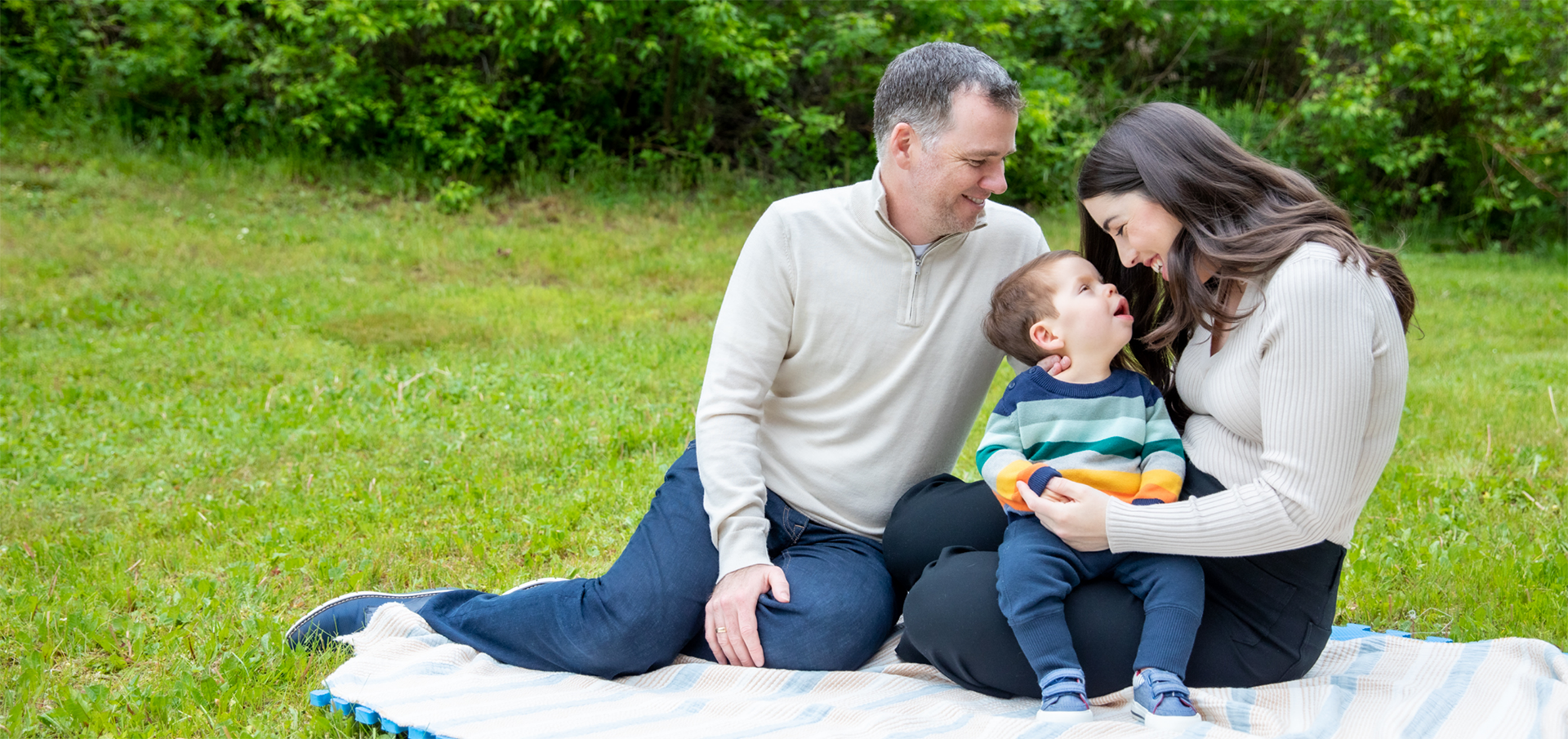 Loving parents, sitting on picnic blanket, smiling down at their child