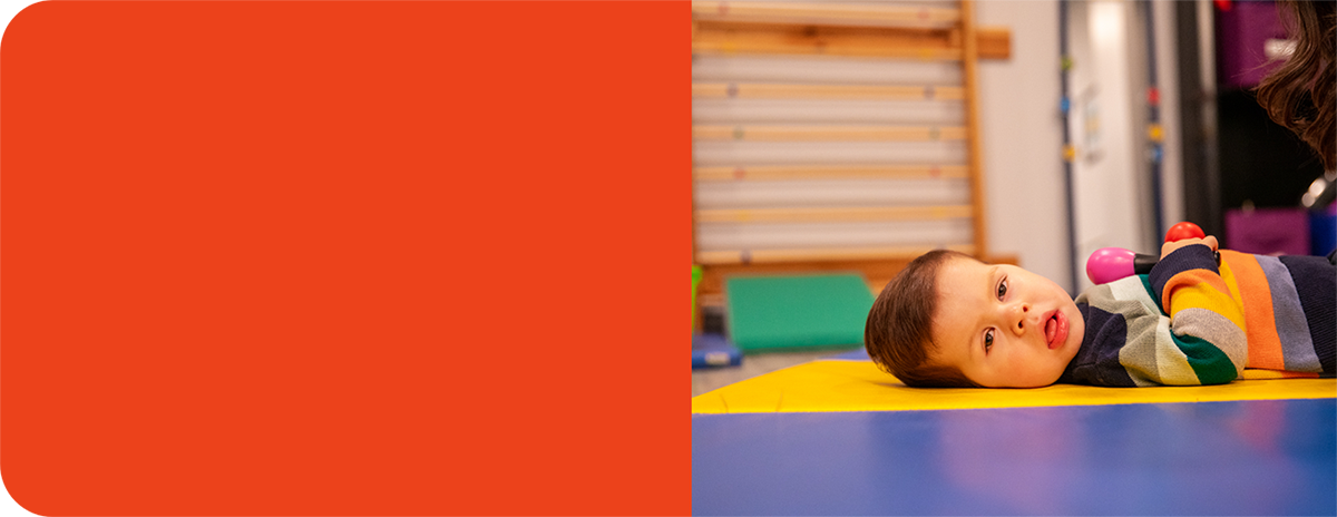 Charlie, a small toddler lying on his back and holding two small shakers