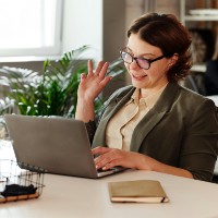 Woman waving at her laptop while on a webinar