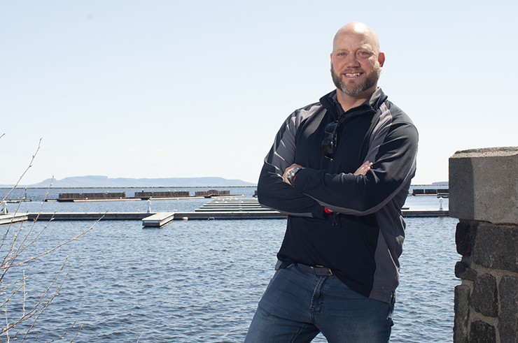 Mike Blackwood - a smiling man leaning on a railing in front of boats at a marina