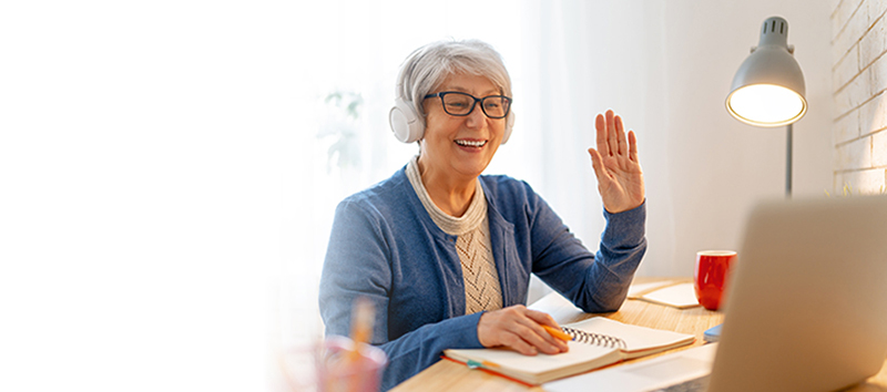 Online Programs - smiling woman with headphones waving at laptop screen