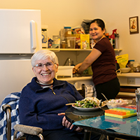 Attendant Care Services - smiling woman with a cane eating lunch with smiling attendant care worker washing dishes