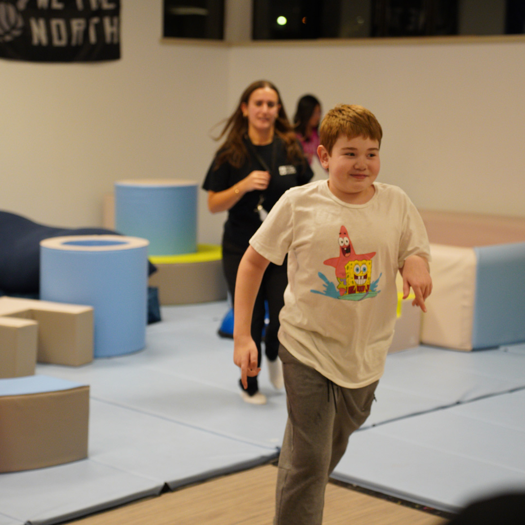 Boy running around a play room with another girl