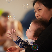 Parent holding their child as they reach towards floating bubbles