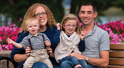 Two kids sitting on their parent's lap on a park bench